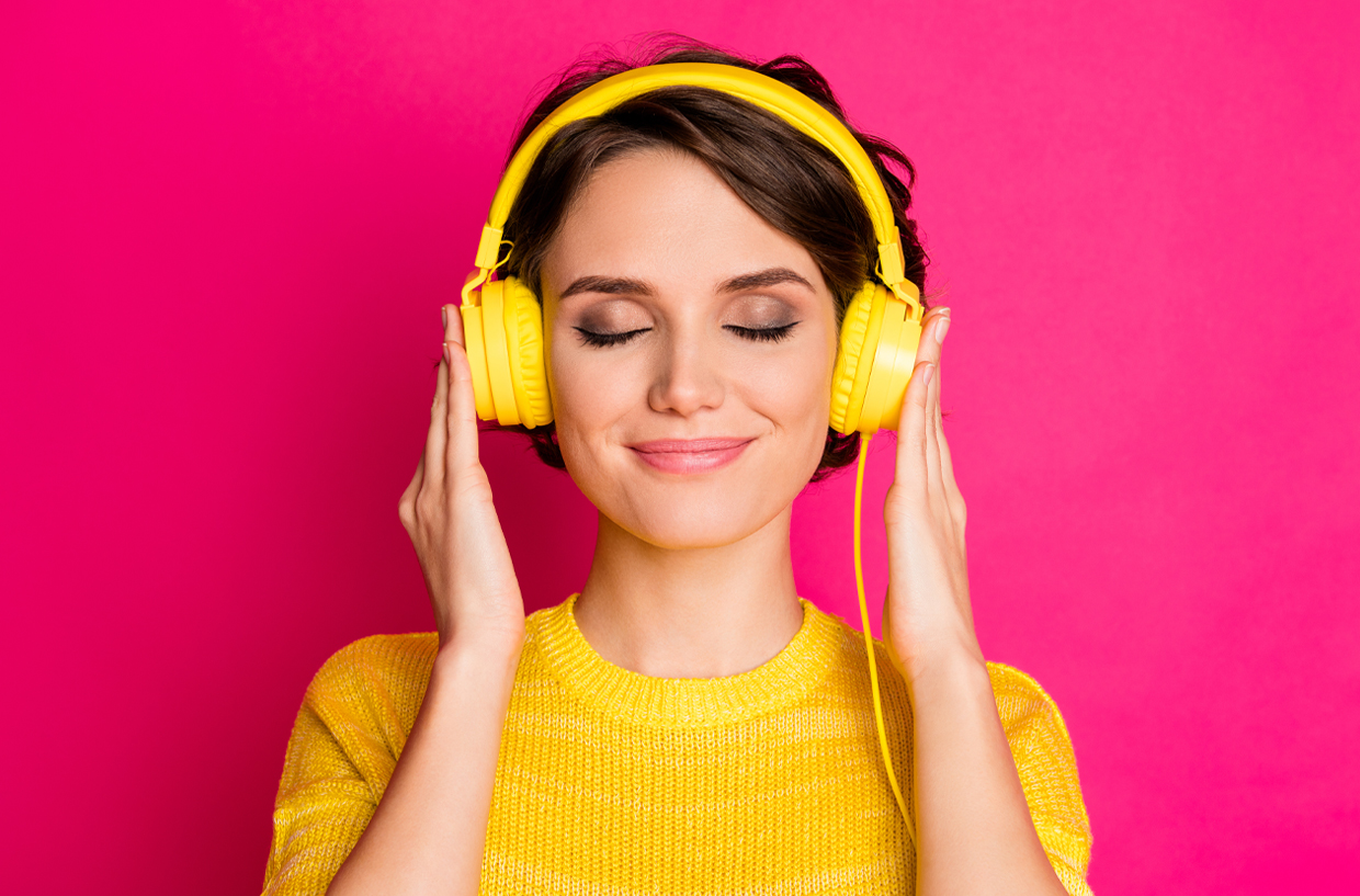 Woman with yellow headphones on a pink background listening happily